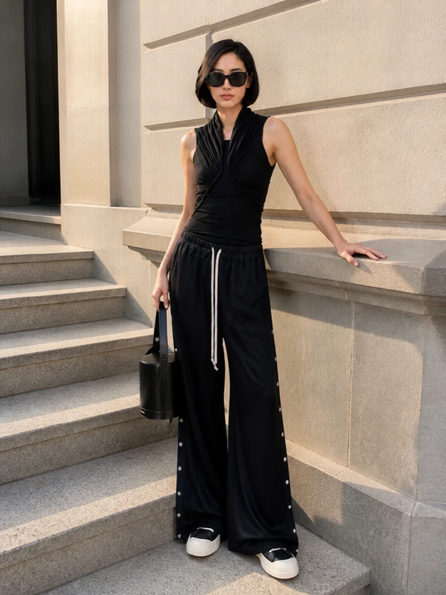 A sculpted black tank slices cleanly against the ultra-wide Rick pants, letting the exaggerated drawcord and pooling hem stay center stage. Graphic black and cream sneakers keep things grounded and easy, while a cylindrical leather bucket and shield shades add just enough structure and attitude for all-day city wear.