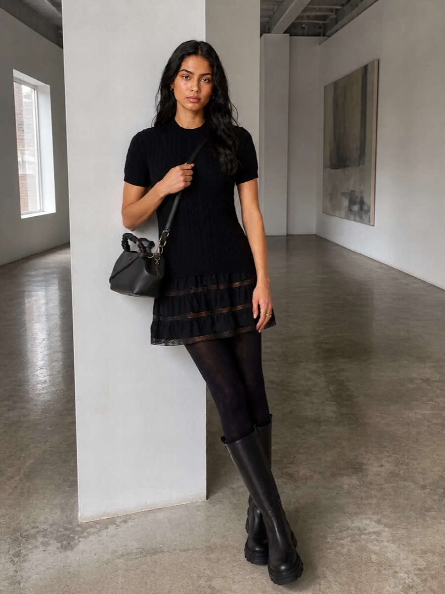 A knit mini with lace inserts is grounded with opaque patterned tights and a chunky knee-high boot for a modern city-romantic feel. The structured black cross-body and tiny bow ring keep the mood intentional but relaxed, ideal from daytime plans to a low-key dinner. All-black textures do the work here so the silhouette stays simple and easy to wear.