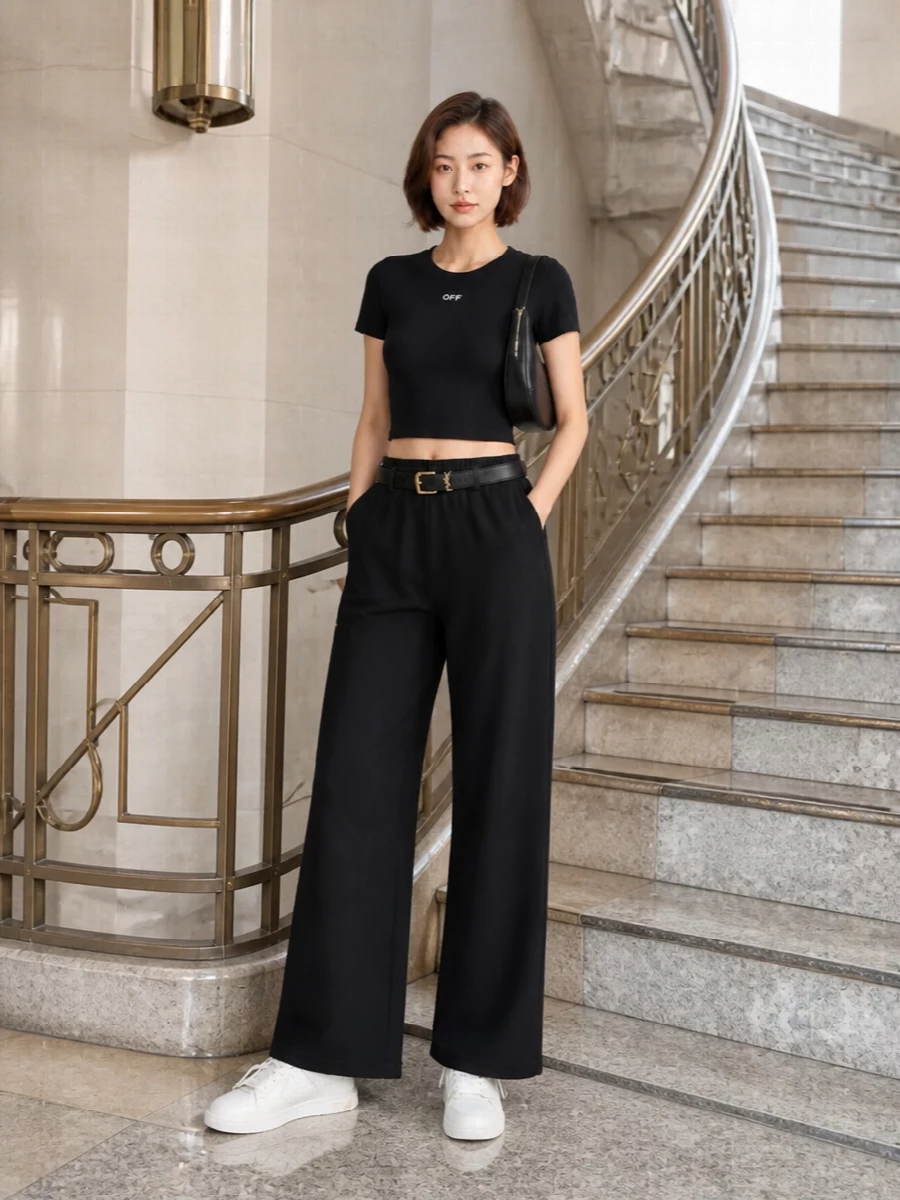 Deep-black wide-leg Off-White pants are paired with a cropped black logo tee to create a long, clean line with a sharp streetwear edge. Off-white low-top sneakers keep the mood casual and graphic, while a curved black Balenciaga shoulder bag and a slim Saint Laurent belt introduce just enough polish for an elevated SS city uniform.