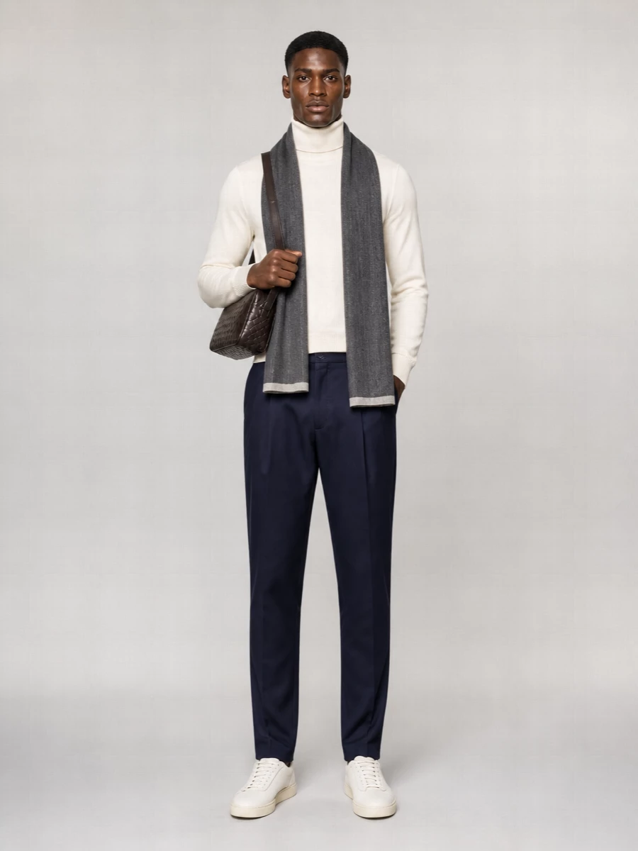 A cream turtleneck and navy pleated trousers create a composed, modern uniform that is sharp enough for the office yet relaxed for dinner. Off-white sneakers keep the mood understated, while the espresso crossbody and slim charcoal scarf add just enough depth and texture to feel considered without breaking the calm palette.