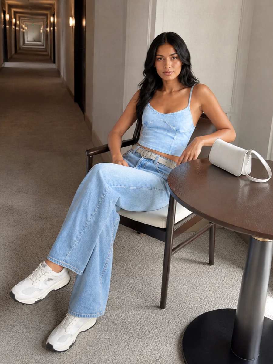 Light-wash wide-leg denim and a sky-blue cami create a soft, tonal base that feels fresh and distinctly Y2K. Off-white runners keep it grounded and easy for all-day wear, while a crisp white shoulder bag and chrome belt sharpen the palette with tight, metallic hits. The result is a relaxed, head-to-toe denim story that reads cool, clean and city-ready rather than costume.