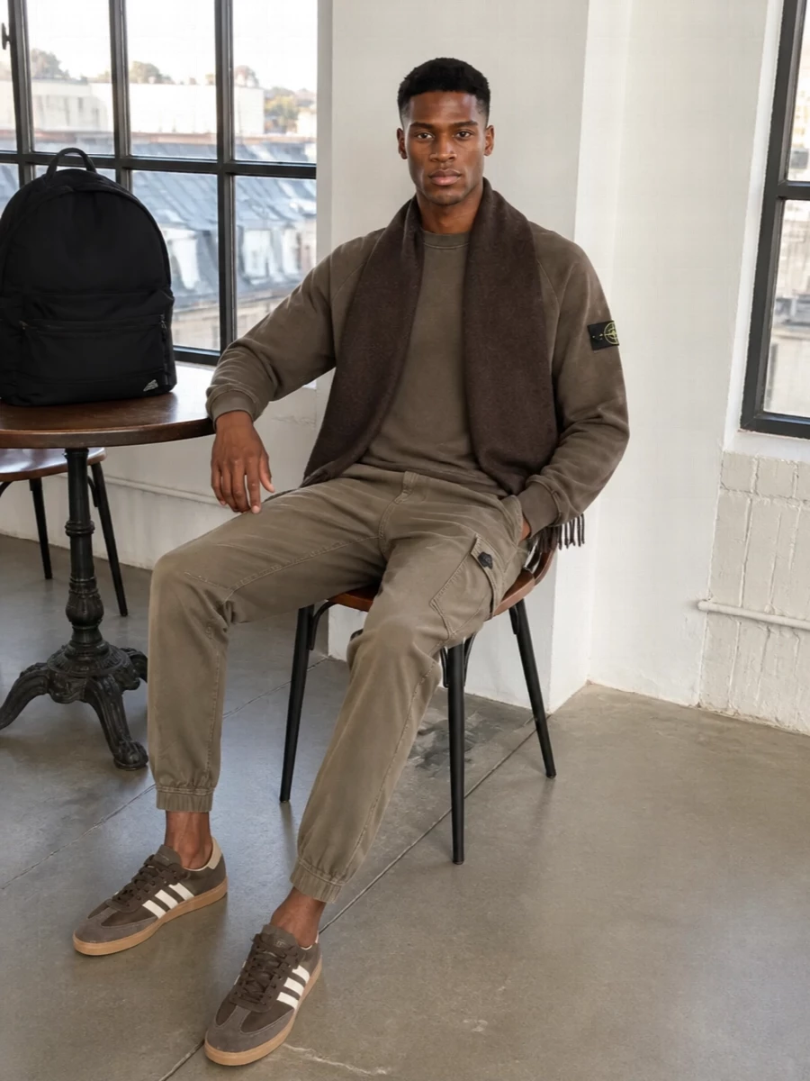 Washed brown on top and taupe cargo joggers create a calm, utility-led uniform that feels considered without trying too hard. Rich brown terrace sneakers echo the earthy tones and keep the line sleek rather than bulky. A black technical backpack and deep brown scarf finish it with quiet function and warmth for city days on the move.