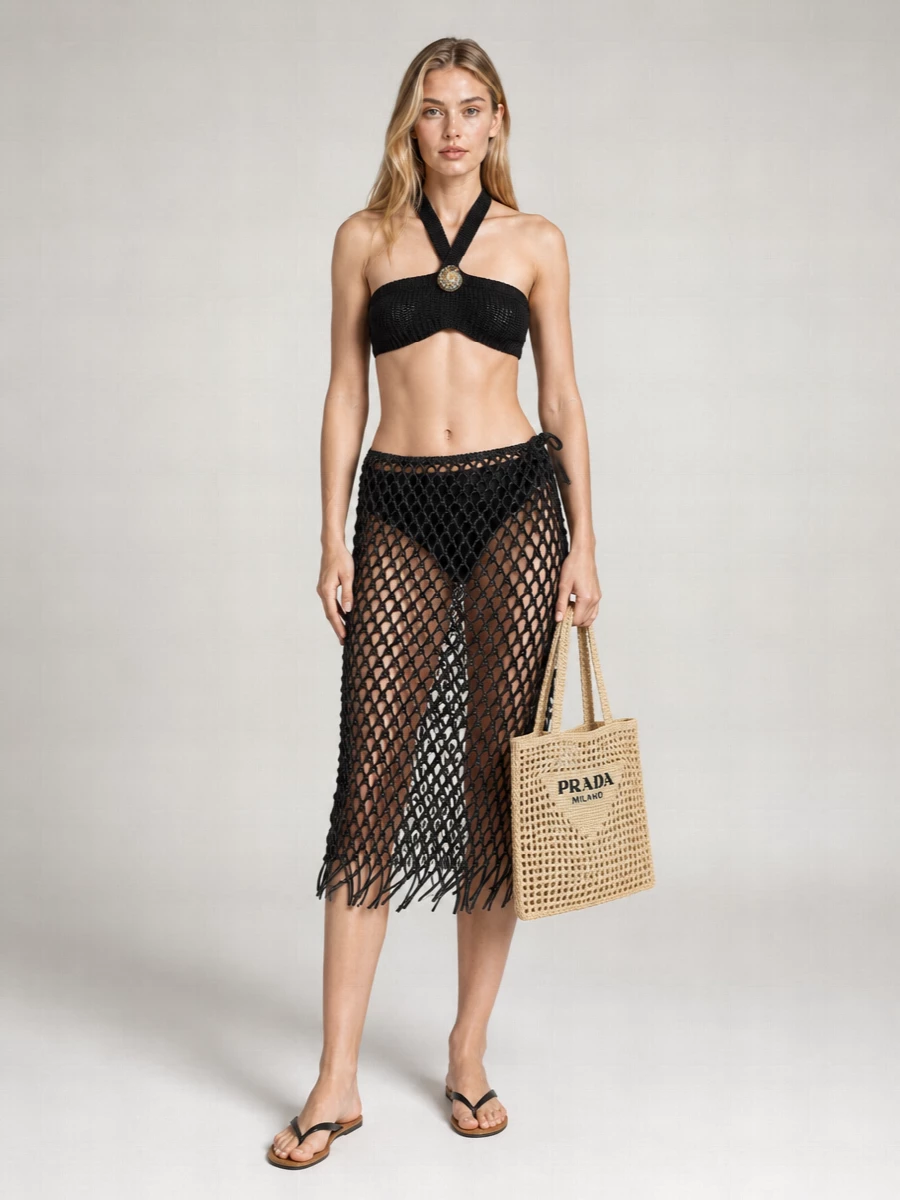 A black open-knit story from hip to halter keeps the mood quietly sensual, with the Alanui bralette and Frankie Shop sarong reading as a single, sculpted swim set. The Row’s slim black thong sandals and Prada’s sand-and-black crochet tote add just enough structure and texture, keeping everything monochrome, modern and boho without sacrificing ease. It is a polished beach-club ensemble that feels considered but never overworked.