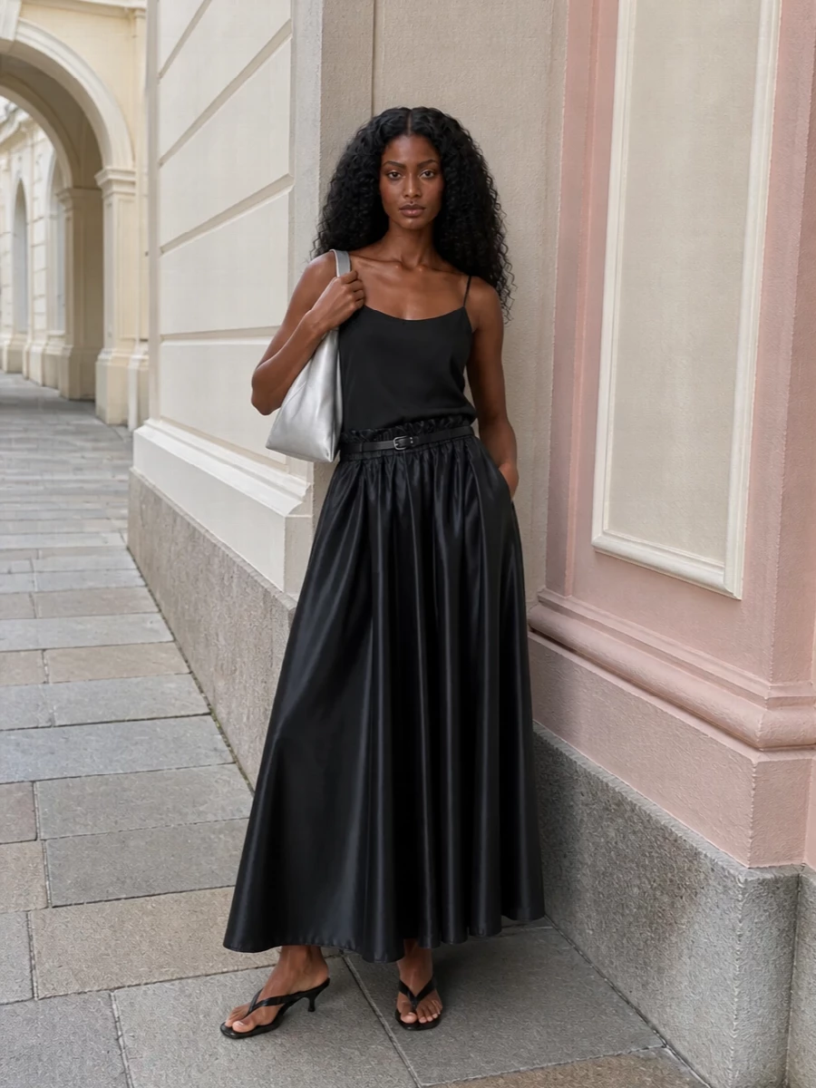 An inky technical maxi skirt teams with a fluid black cami for a clean, almost liquid column that feels modern and quietly dramatic. A sharp black kitten-heel thong keeps it city-ready without breaking the line, while a sculptural silver hobo and slim black belt pick up the skirt’s gunmetal sheen for a cohesive, minimalist finish. The result is refined streetwear that can move from daytime galleries to low-key dinners with a simple change of attitude, not pieces.