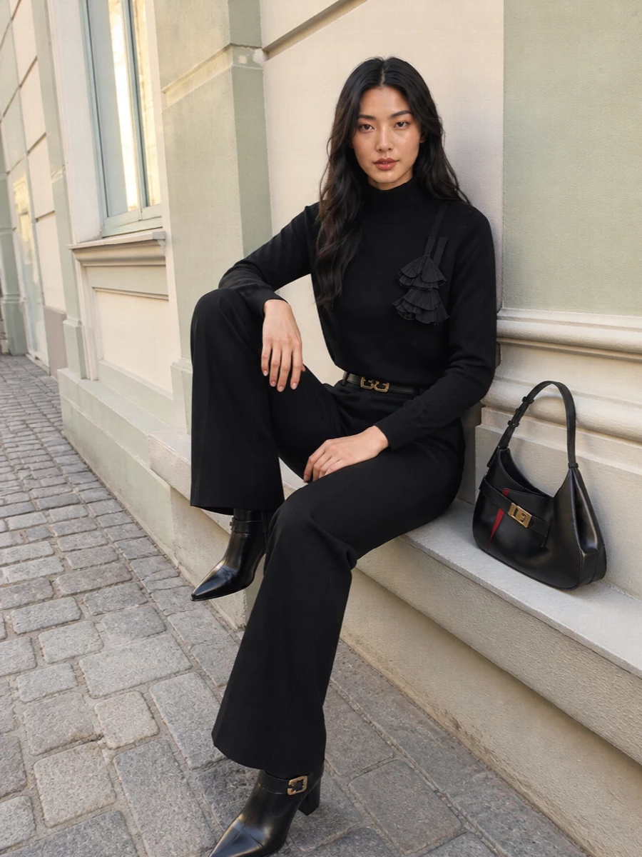 Ferragamo’s high-rise flared trouser is paired with the sculpted black mock-neck knit to create a long, monochrome line with just a hint of shoulder texture. A pointed black ankle boot keeps the hem clean and directional, while a structured black shoulder bag and a slim Gancini belt add coordinated gold accents for a quietly luxurious city uniform. The result is precise, elongating and ready for anything from desk to late dinner with a simple change of jewelry or lip.