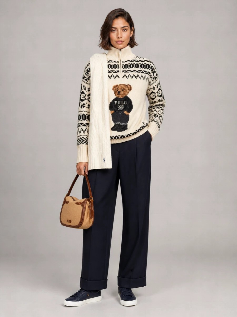 A cream Polo Bear half-zip is grounded with sharply cut navy pleated trousers for a relaxed, quietly polished winter take on prep. Navy sneakers keep the mood sport-influenced yet clean, while the camel shoulder bag and soft cable-knit scarf pull in warm, heritage notes that echo the sweater without overwhelming it. The result is cozy, graphic knitwear styled with tailored ease for coffee runs, travel days, and casual dinners alike.
