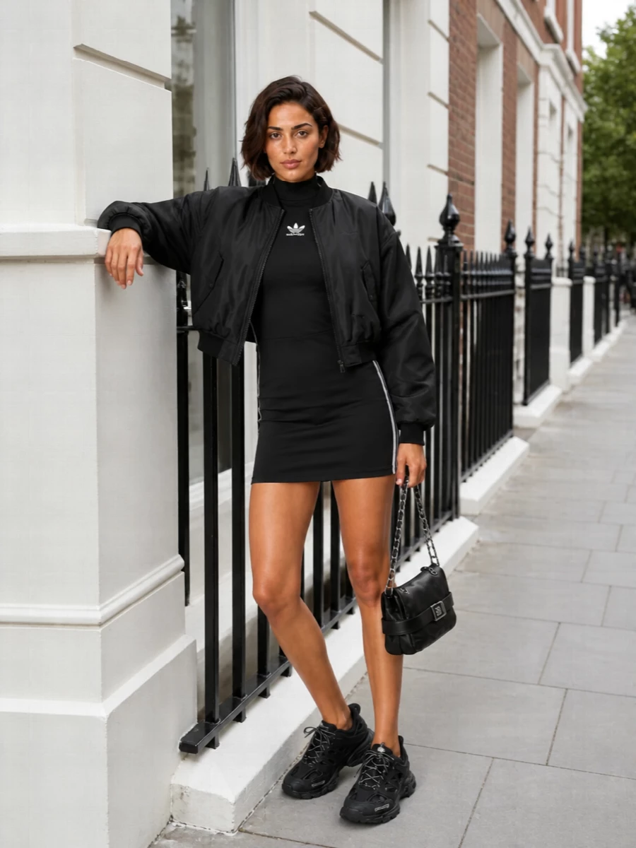 I’m building around the dress rather than top and bottom, because its track-sport bodycon line gives a stronger, uninterrupted base under the cropped Balenciaga bomber. The result is a monochrome, club-adjacent street outfit that feels intentional from every angle, with the technical runners and chain-strap bag pushing it into that recognisably Balenciaga, city-at-night mood. It is athletic, graphic and clean, without a single piece fighting the bomber’s volume or minimalism.