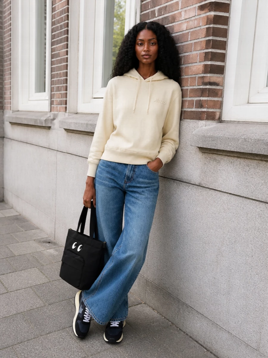 Autry’s buttercream hoodie and the faded wide-leg Ami denim lean into an easy, sport-led weekend mood that feels considered but unfussy. The palette quietly picks up the sneaker’s buttercream sole and navy-black body without going matchy, while the wide leg keeps the retro runner feeling balanced and modern. Anya Hindmarch’s graphic tote finishes it with a relaxed, city-ready attitude that still has personality.