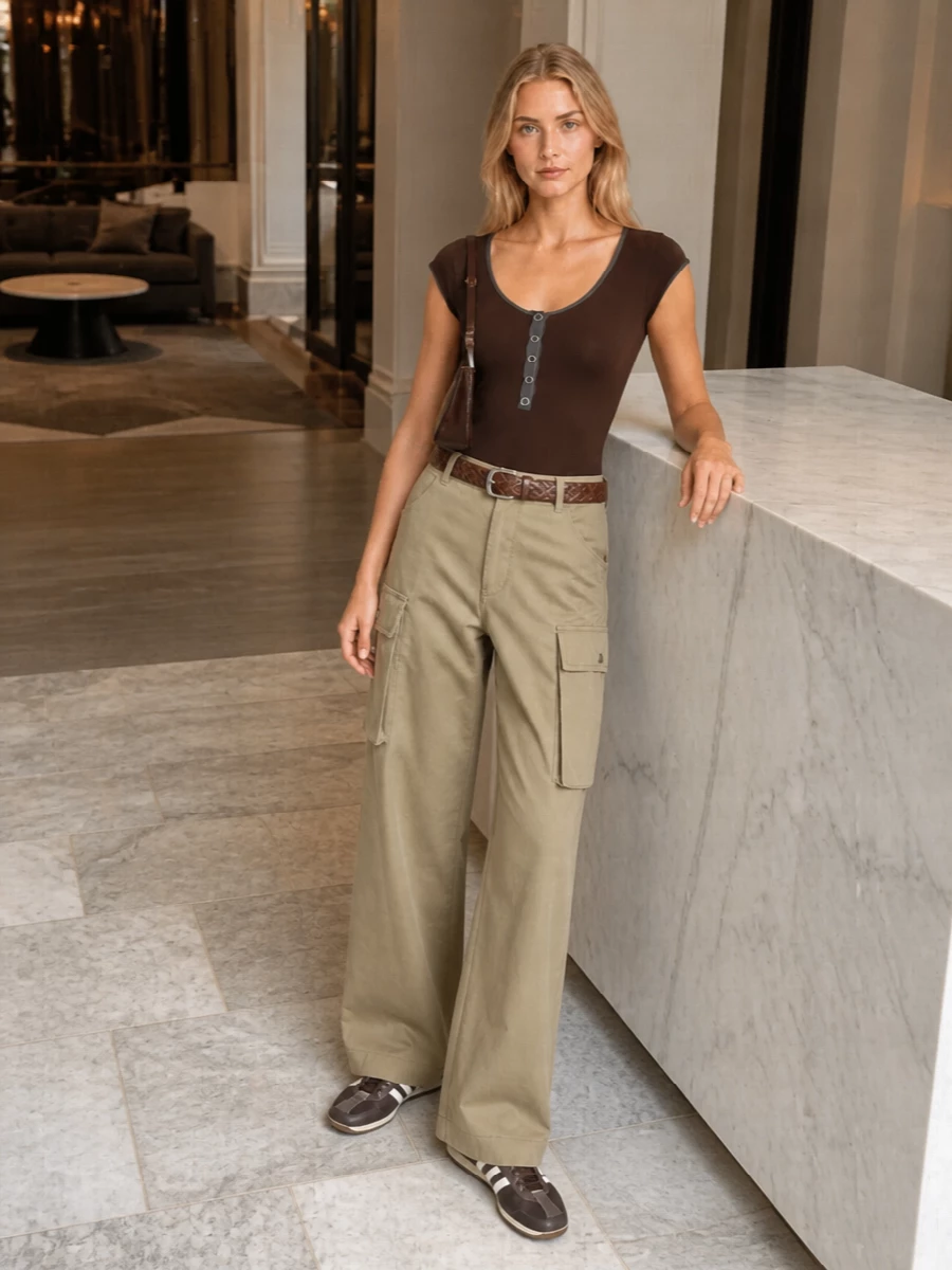 A graphic chocolate bodysuit grounds roomy khaki cargos for a clean, Y2K-leaning city uniform. Retro-slim brown sneakers keep the line sleek rather than bulky, while a glossy Jacquemus shoulder bag and braided belt pull the brown accents into a considered, low-key statement. The result is relaxed but precise, ideal for warm days that still need a bit of attitude.