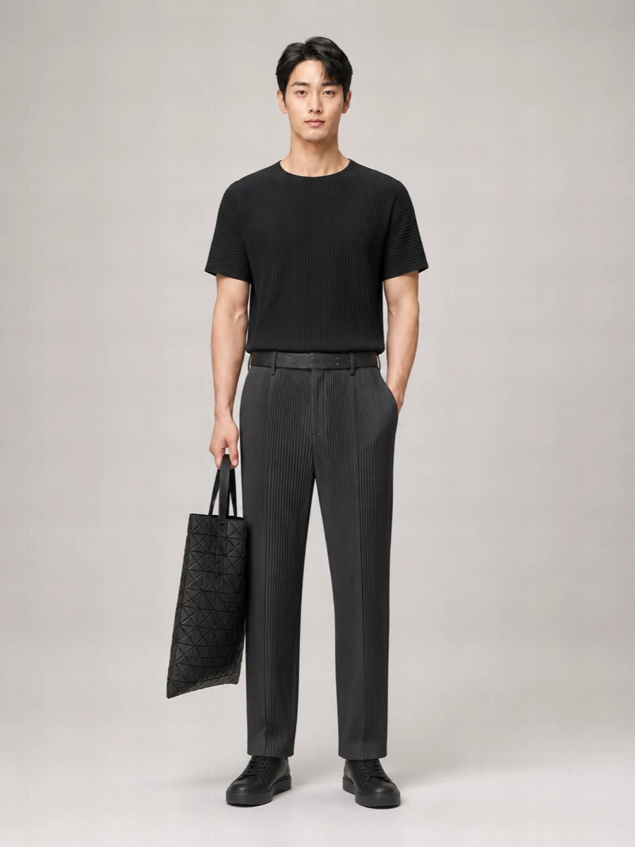 Head-to-toe pleated texture in charcoal and black creates a calm, graphic column that feels sculptural but relaxed. The straight leg keeps the proportions easy around the boxy tee, while the all‑black leather sneaker and geometric tote stay quiet but intentional. It is a city uniform that reads thoughtful and technical without a single loud note.