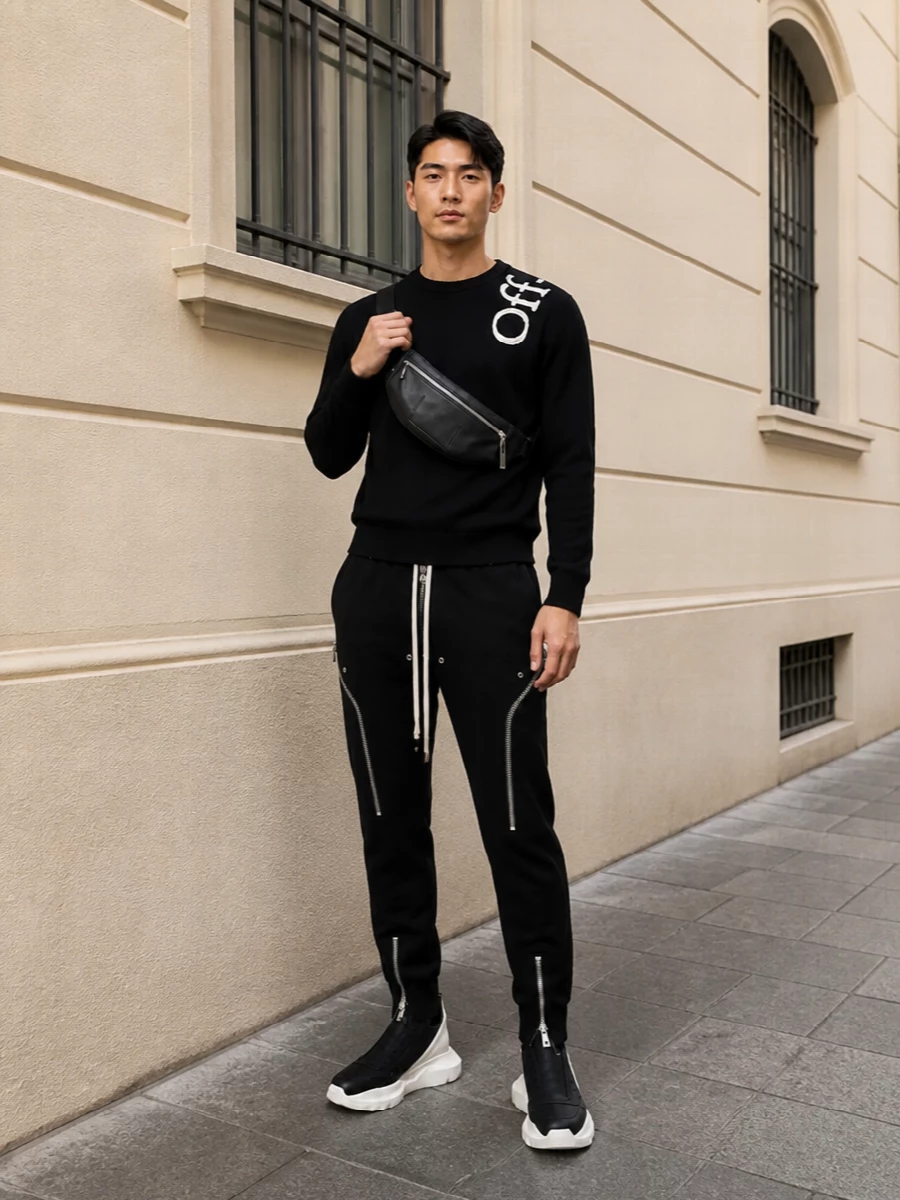 Off-White and Rick Owens meet in a tight monochrome story, with the graphic crew grounded by sculpted, zip-heavy joggers. Chunky high-top sneakers and a razor-clean belt bag keep the silhouette athletic and urban while staying firmly luxury. The result feels like a considered street uniform you can wear from studio days to late nights without changing a piece.