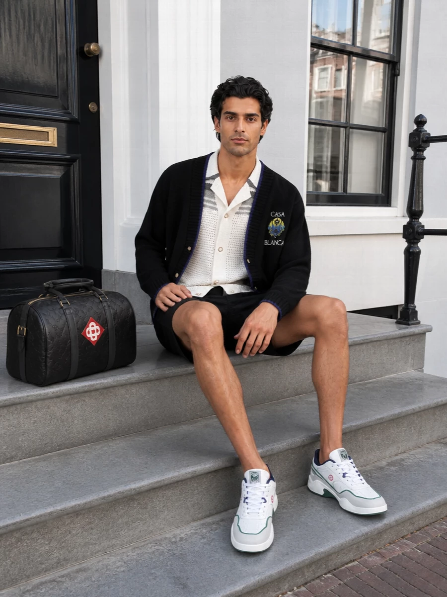 Casablanca’s black varsity cardigan sits over a cool-toned crochet shirt and jacquard shorts, all in a tight black, ivory and grey palette with subtle crest notes. Retro court sneakers and a structured duffle keep it in that sweet spot between city coffee run and impromptu weekend escape, with texture doing the talking instead of print overload.