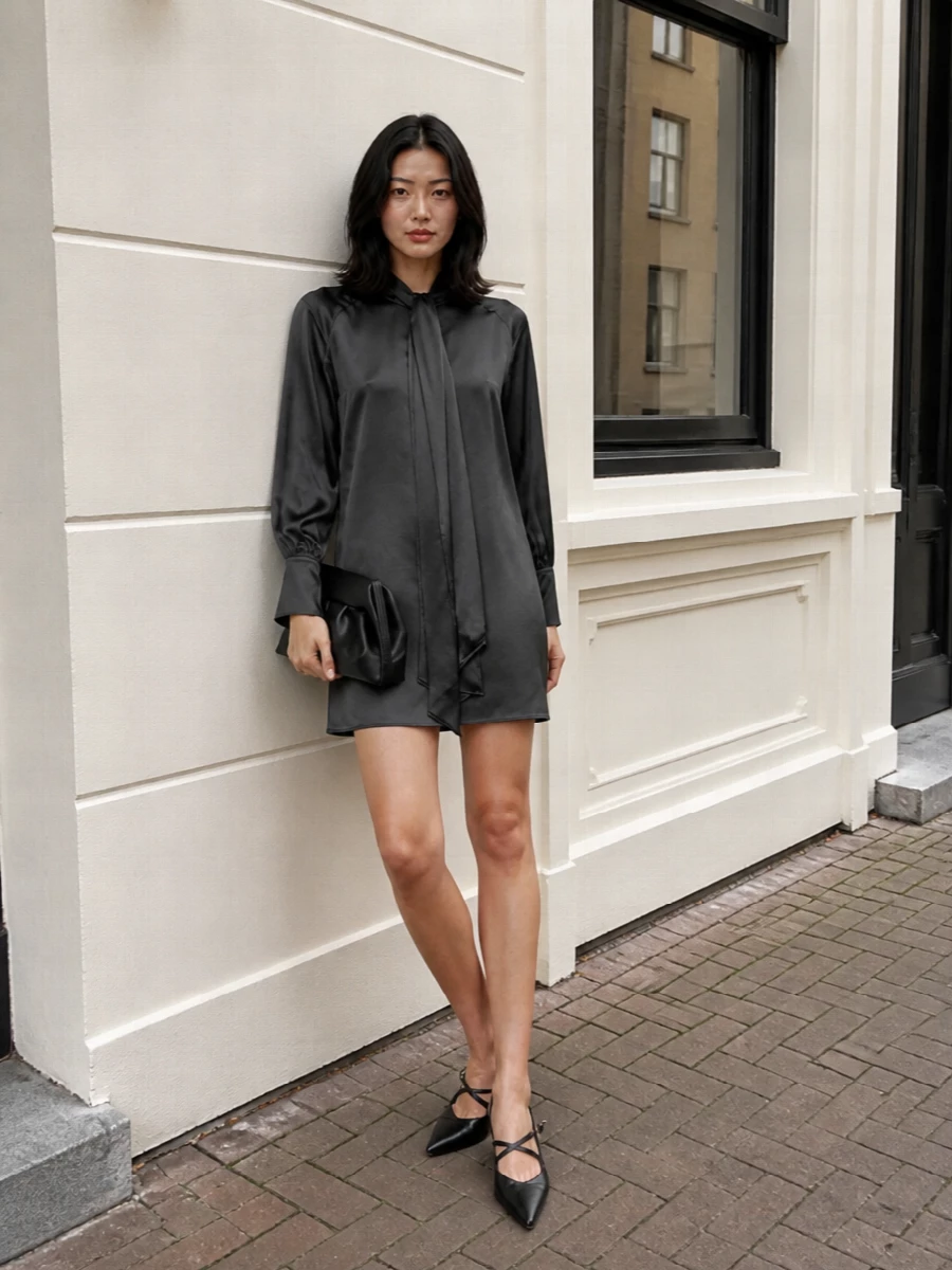 Charcoal satin, sculpted black slingbacks and a structured clutch create a low-key evening ensemble that feels considered rather than loud. The long tie neck and sheer tonal scarf add just enough movement, keeping the silhouette clean while the textures do the talking.