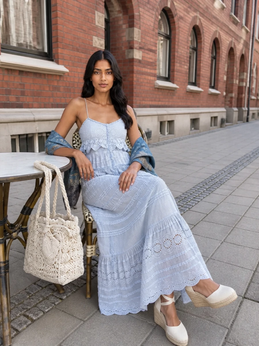 A pale blue tiered maxi is grounded with soft ivory espadrille wedges for an easy, sunlit sense of height. An ivory crochet tote keeps the textures romantic and airy, while a misty blue stole adds a poetic wash of color at the shoulders. The result feels ideal for garden parties, coastal terraces, or any warm afternoon that drifts into evening.