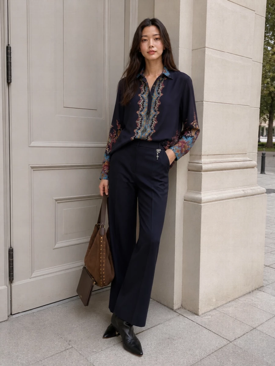 A midnight paisley shirt falls over precise navy wide-leg trousers for a column of color that feels romantic yet composed. Slouchy black ankle boots and a suede hobo bag bring in that soft, boho ease while keeping the mood refined for city dinners and late autumn evenings.