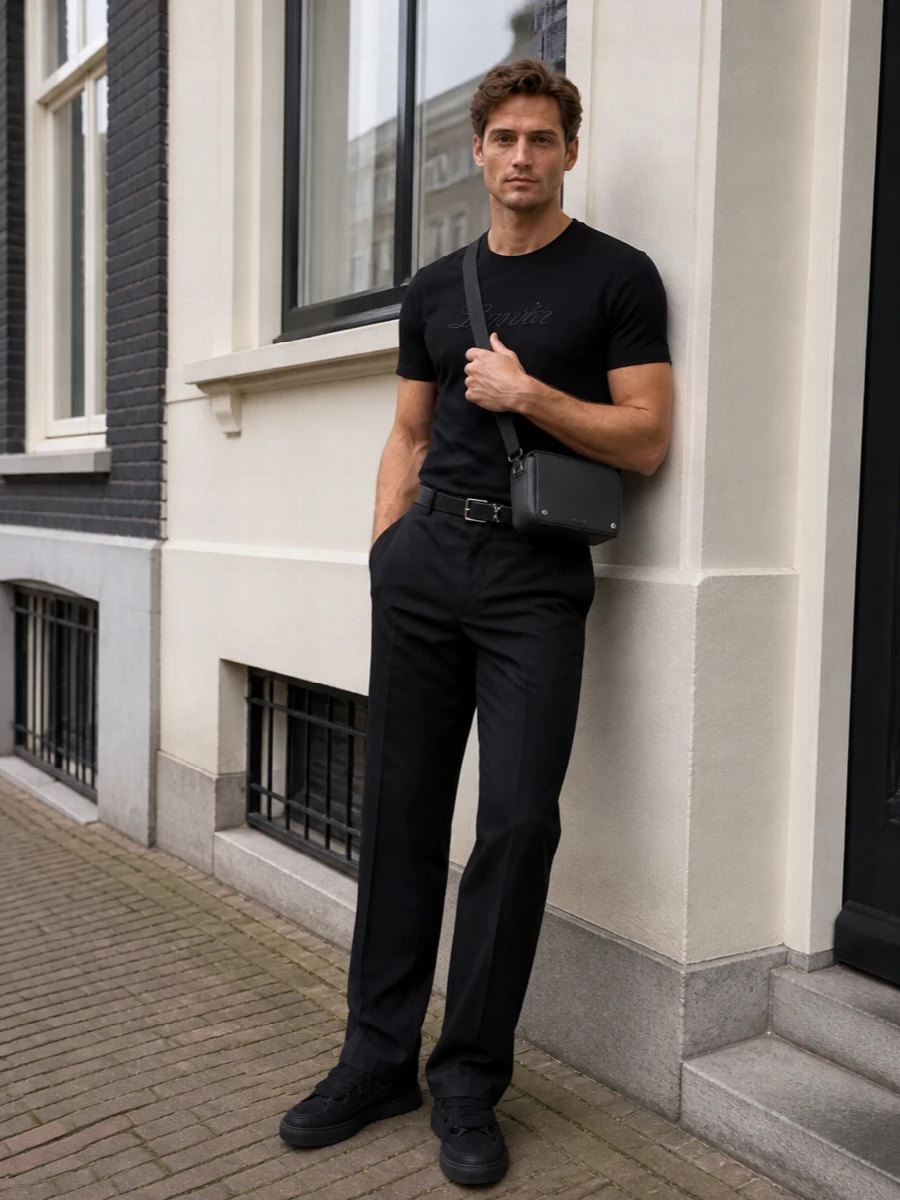 A black-on-black palette keeps everything focused on line and texture, from the tonal-script tee to the clean straight-leg trouser. Sculpted Lanvin sneakers add subtle volume at the ground, while Loewe’s structured crossbody and a slim Saint Laurent belt bring just enough hardware to signal intent without competing for attention. It is relaxed enough for the city all day yet considered enough to carry straight into a low-key dinner.