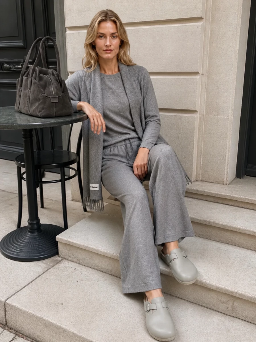 A tonal grey story keeps this relaxed wide-leg knit feeling intentional rather than purely lounge. The subtly sparkling sweatshirt, soft clog and suede shoulder bag play with texture in the same quiet register, so the whole outfit reads calm, considered and ready for a coffee run or a low-key meeting. The linear scarf finishes it with a gentle vertical line that flatters the easy silhouette.