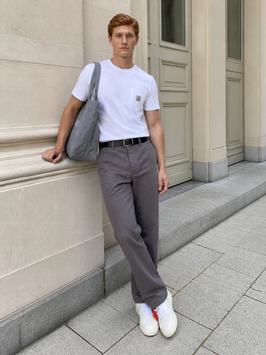 A clean white pocket tee meets muted taupe-grey straight legs for a calm, utility-led base that feels ready for city days. Off-white Off-White sneakers echo the tee and quietly sync their bold tag with the Carhartt logo hit, while a striped tote and slim black belt keep everything grounded and functional without breaking the minimalist rhythm.
