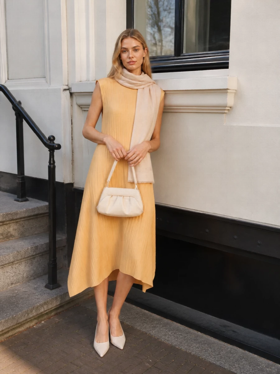 Soft apricot pleats are framed with ivory accessories for a calm, luminous palette that feels polished without effort. A low kitten heel and compact pleated bag keep the lines clean and modern while remaining easy to wear all day. Gold studs and a blush scarf warm everything up just enough, so the dress stays the quiet focal point.
