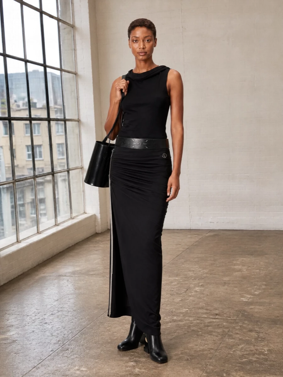 A long, ruched black column anchored with an asymmetric tank creates a dark, continuous line that feels precise rather than fussy. Sculptural ankle boots and a structured gloss-black bucket bag push it firmly into urban night territory, while a wide, pared-back belt quietly sharpens the waist. The result is pure Rick energy, distilled into a minimal, gallery-to-after-hours uniform.