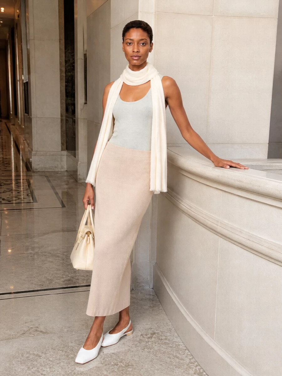 Soft heather grey and pale beige knits are paired to create a quiet column that feels relaxed yet intentionally put together. The ribbed maxi skirt sharpens the cocooning tank, while the flat white slingback and structured buttercream bag keep the mood clean, modern and easy for warm days. It is a tonal, minimalist combination that reads as calm luxury rather than loungewear.