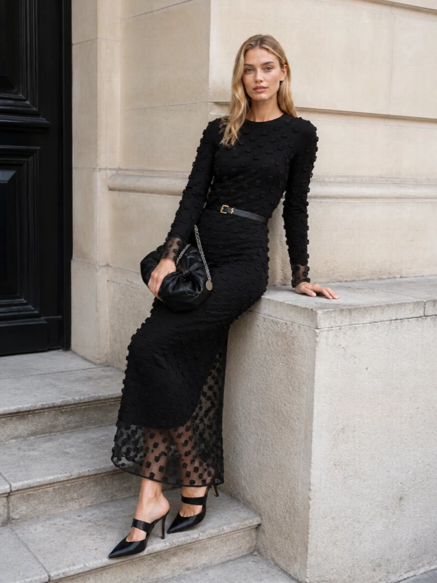This look leans into dark, modern romance: the sheer, textured Sportmax maxi is anchored by sharp black satin Manolo mules for a long, uninterrupted line. A sculptural knotted black clutch adds a discrete focal point, while a slim black Saint Laurent belt introduces just enough gold hardware to keep the mood polished yet understated. The result is a quietly dramatic evening outfit that feels architectural rather than overtly feminine.