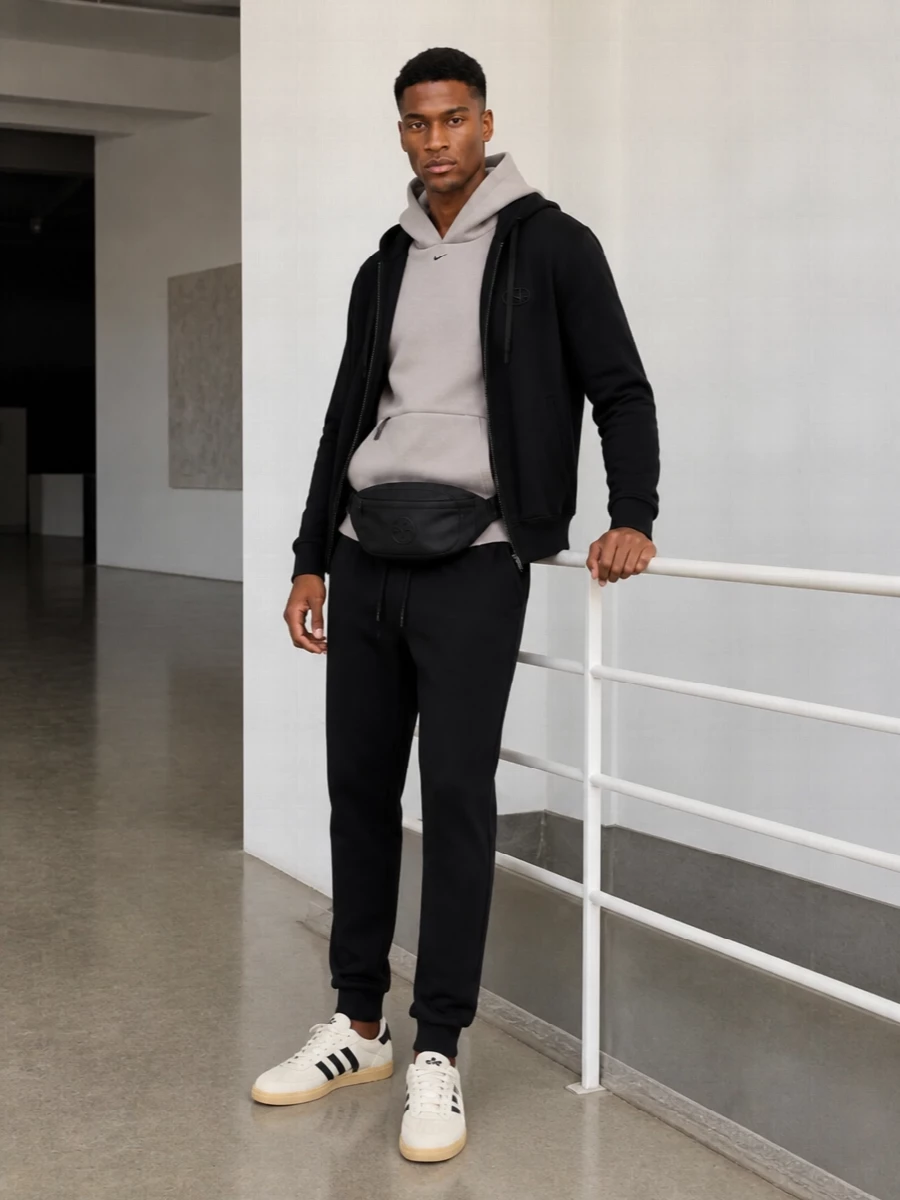 A pared-back city set built around deep black layers, with a soft taupe hoodie bringing a slightly romantic warmth to the palette. Clean black track pants and a compact Moncler belt bag keep the profile streamlined, while cream Adidas terrace sneakers add just enough contrast to feel considered rather than stark. The result is modern street sport that feels quietly emotive, ideal for cool-season days that move from commute to late-night walks.