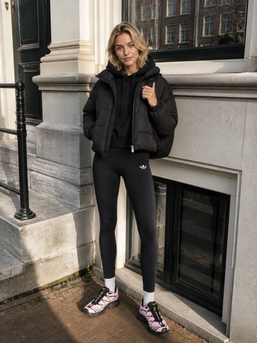 I’m anchoring this around the top and bottom rather than a dress so the puffer can stay in its natural habitat of technical layers and easy movement, not fighting a going-out knit. A black cropped Y-3 hoodie and Adidas leggings create a streamlined sport base under the jacket, then pink Salomon runners and a black A.P.C. backpack push it toward modern city-trek energy. The result is a tight, mostly monochrome palette with one soft color accent, all reading high-function, high-style streetwear for cold days on the move.