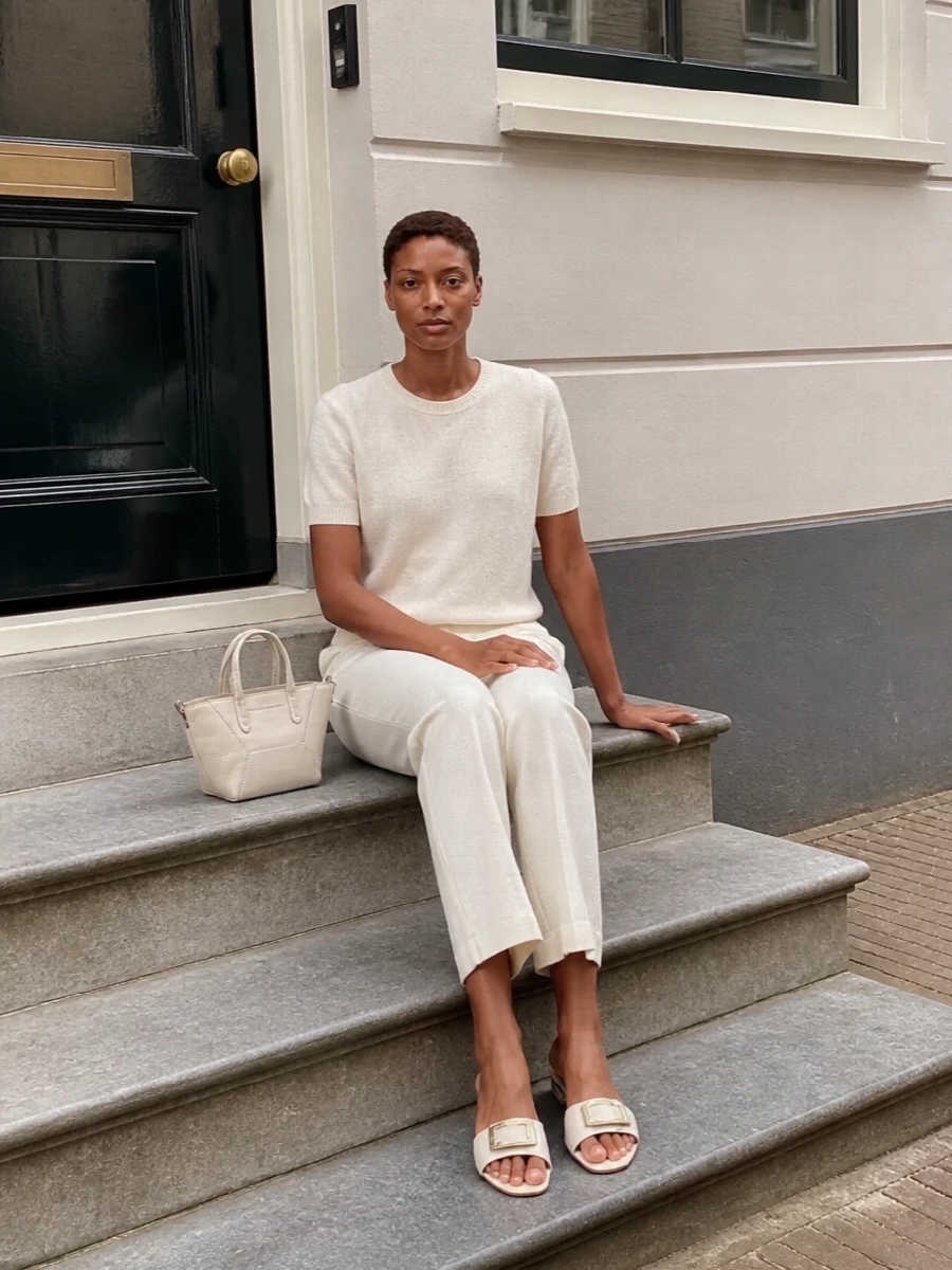 An ivory-on-ivory pairing keeps the focus on texture, from the softly shimmering knit to the fluid straight-leg trouser. The clean lines are gently sharpened by a structured mini bag and a low-heeled slide, creating a calm, refined outfit that works from daytime appointments to terrace dinners. Subtle hardware and tonal shades do the work of jewelry without breaking the minimalist mood.