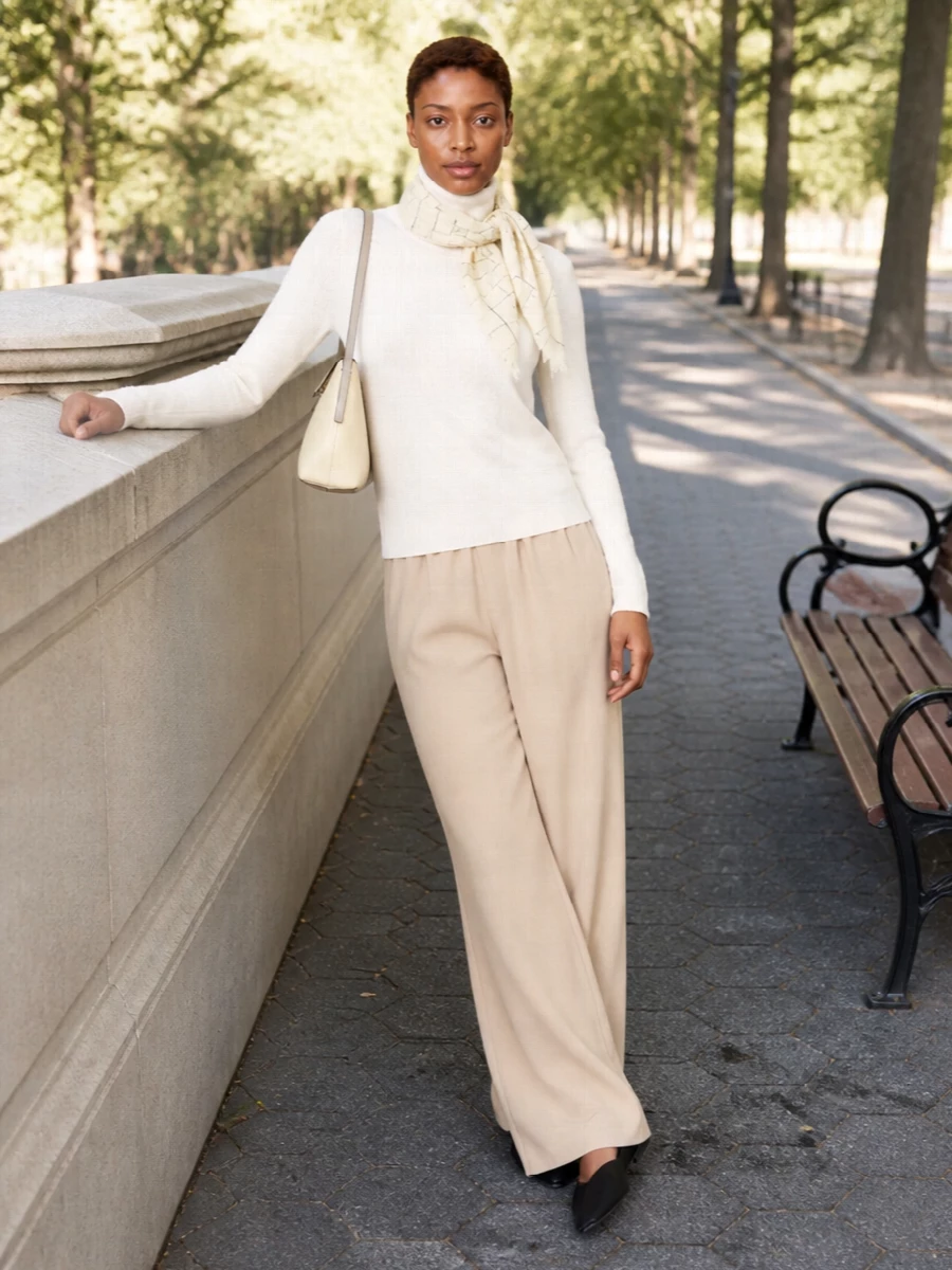 Soft ivory and warm beige sit together in a calm, tonal pairing that feels relaxed yet considered. The fluid wide-leg trouser and easy turtleneck create a long, unfussy line, grounded by a sharp black flat for just enough definition. A buttercream shoulder bag and a checked scarf at the neck or handle finish the outfit with quiet structure and texture rather than contrast.