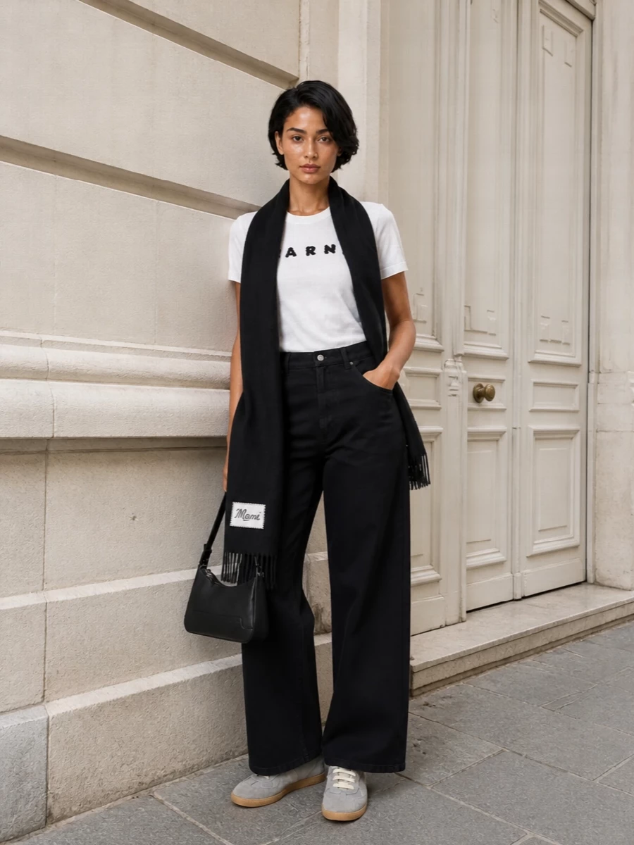 A Marni logo tee meets Margiela-inspired wide-leg tailoring for a clean, graphic city uniform in soft white, charcoal, and black. Grey low-top sneakers keep the proportions grounded and relaxed, while the slim black baguette bag and long scarf sharpen the monochrome palette without disturbing its ease.