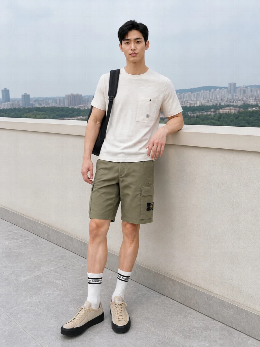 Stone Island cargo shorts meet an off white patch pocket tee in a clean, utility driven pairing that feels sharp but easy for warm city days. Neutral toned technical sneakers keep the line streamlined and agile, while a black backpack and striped socks add just enough contrast to ground the palette without breaking the minimal mood.