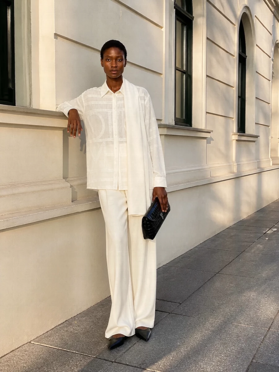 A tonal ivory column in sheer geometry and tailored wide-leg trousers feels calm yet precise, the texture doing the talking while the palette stays restrained. Black pointed flats and a sculpted croc clutch add just enough graphic contrast to keep it urban and sharp without disturbing the shirt’s quiet detail.