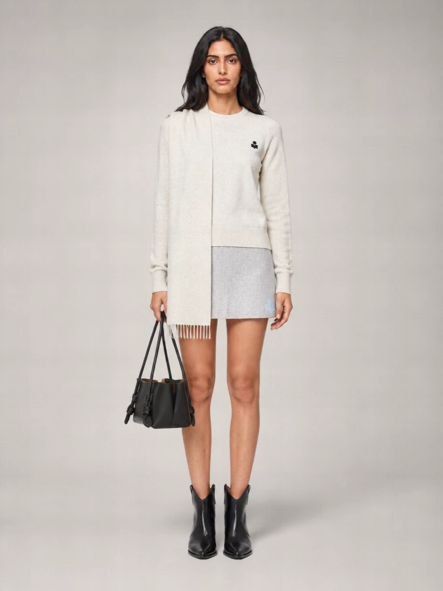 Soft oatmeal knit and heather-grey mini skirt set a relaxed Parisian baseline, with clean lines and subtle logo details keeping everything unfussy. Pointed black Chelsea boots and a structured black shoulder bag add just enough definition so the proportions feel sharp, not sweet. An ecru scarf finishes the mix with extra texture and warmth while staying firmly in the same gentle neutral palette.