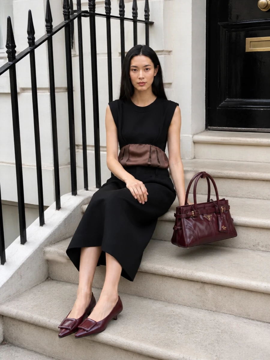 A sculpted Marni midi in black and chocolate sets a modern, gallery-ready base that lets the Prada oxblood bag do the talking. The precise tailoring and clean neckline feel quietly powerful, while the burgundy Roger Vivier kitten heels softly echo the bag’s richness without breaking the restrained palette. Choosing the dress route keeps the silhouette sleek and uninterrupted, ideal for showcasing structured accessories and fine jewelry.