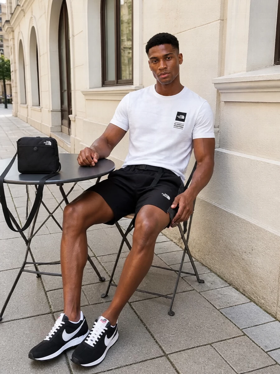 A soft white graphic tee sits against sharp black technical shorts for a clean, sport-driven base. Retro black-and-white runners and a compact crossbody keep everything fast, minimal and city-ready. The result is an easy warm-weather uniform with just enough trail DNA to feel purposeful, not precious.