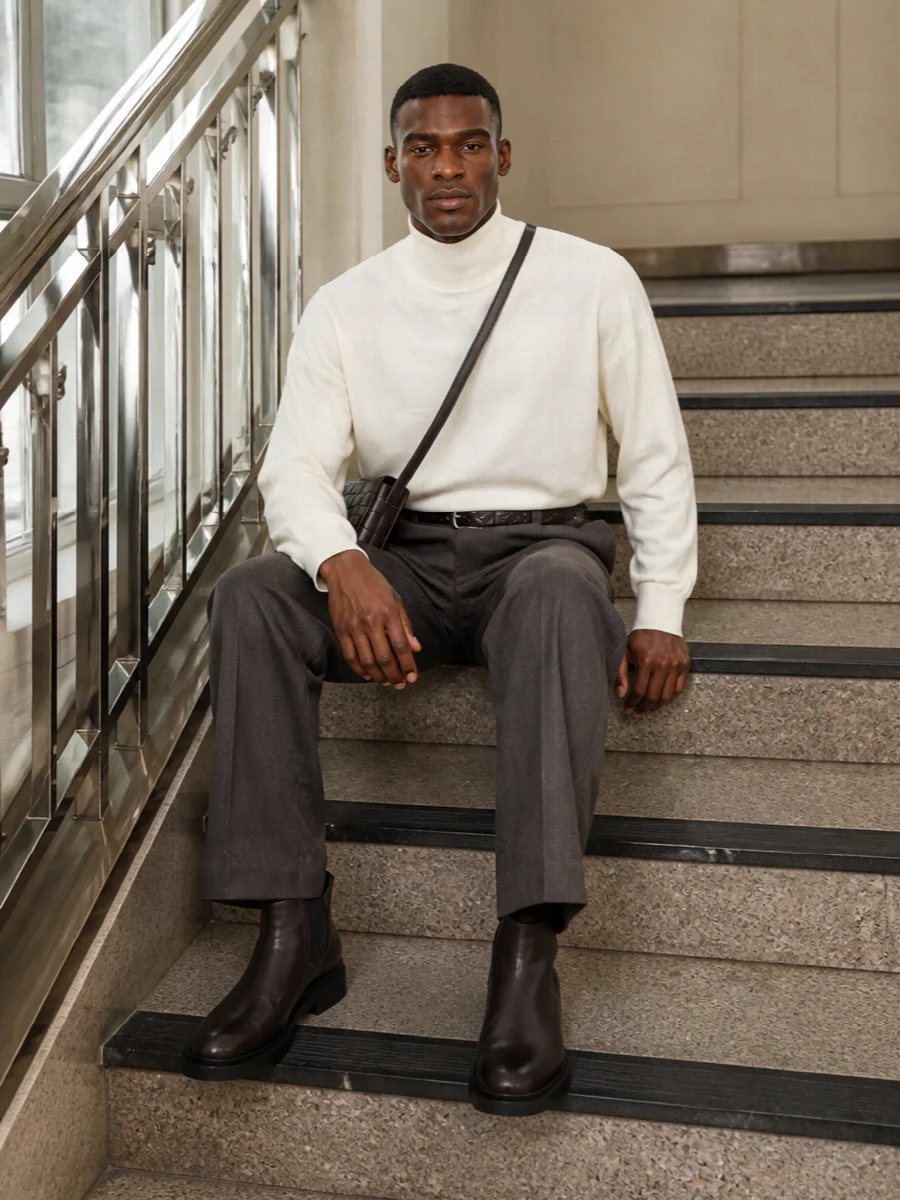 A high-waisted charcoal trouser meets an ivory turtleneck for a clean, elongated silhouette that feels confident without show. Dark brown Chelsea boots and an espresso belt ground the proportions, keeping everything in a tight, quietly rich palette. The compact crossbody adds just enough texture to signal intention while staying firmly in the background of the outfit.
