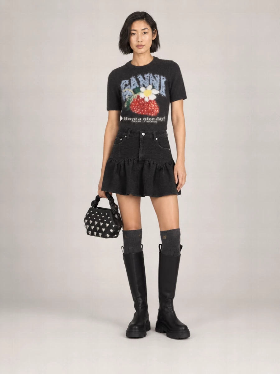 A flippy high-waisted mini meets a cropped fuzzy graphic knit for a tight, monochrome base that still reads playful. Chunky knee-high boots and charcoal socks bring the stomp, while a studded mini bag adds just enough hardware to tip this into late-afternoon-to-night-out territory without losing its easy, city edge.