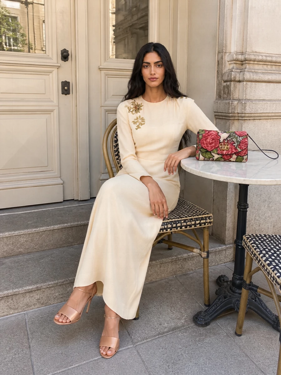 This pairing leans into soft, romantic evening dressing with a long embroidered buttercream column that echoes the clutch’s florals without adding more print. The clean neckline and fluid silhouette keep the composition minimal, while nude heels and the richly textured red rose bag provide just enough drama for formal dinners or winter weddings. Choosing the dress path over separates keeps the focus on texture and line, letting the bag read as a considered jewel rather than one pattern among many.
