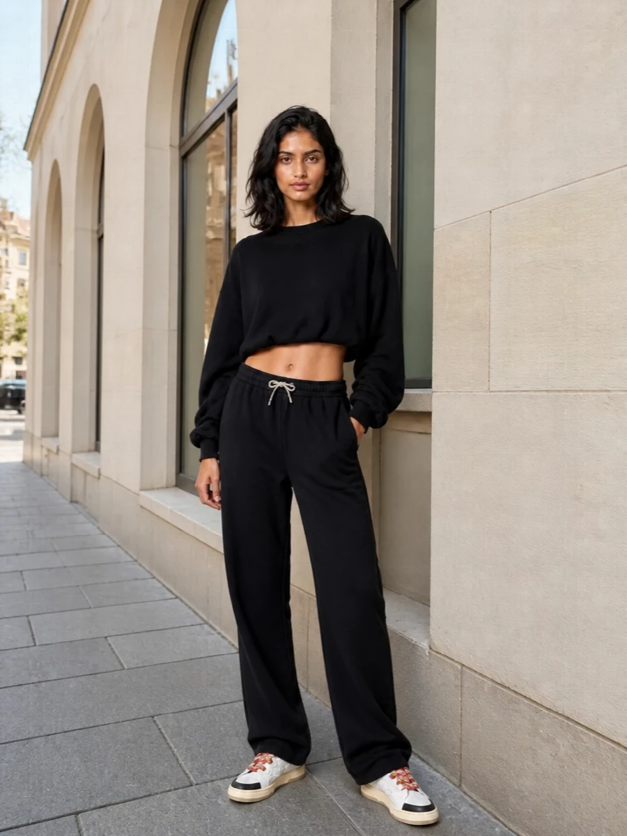 A cropped black sweatshirt with ruched sleeves sits over fluid black track pants so the Lanvin sneakers become the graphic punch of color. The proportions feel relaxed but intentional, with volume at the leg and a clean, boxy top that shows just enough waist. The neutral base lets the red chevron laces and subtle sport details read strong without overwhelming the outfit.