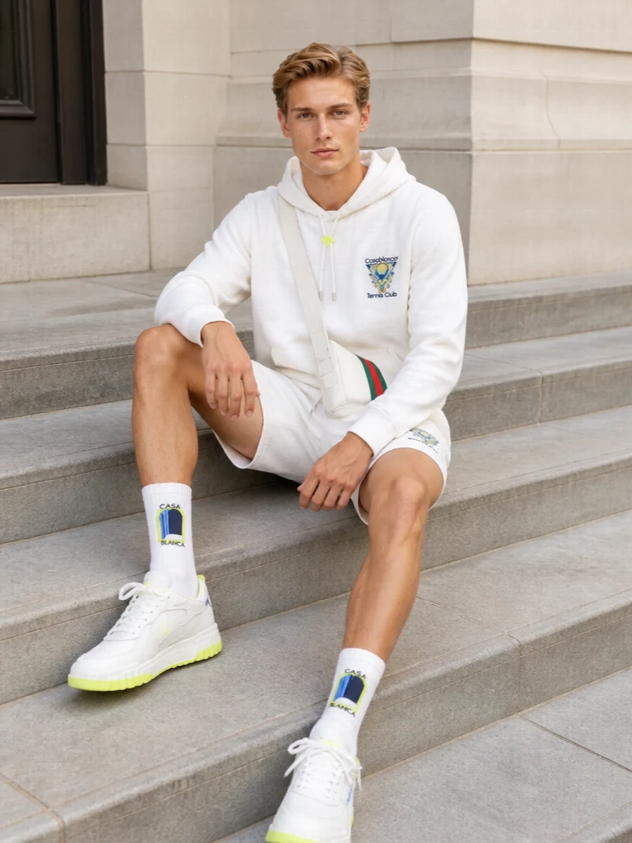 A clean Casablanca tennis story built around white, tennis blue and neon hits, this outfit feels like a modern country-club uniform for the city. Matching hoodie and shorts keep the silhouette simple, while the neon-trimmed sneakers and branded socks bring just enough graphic attitude. The Gucci crossbody finishes it with a subtle nod to old-guard heritage within a very current resort-sport palette.