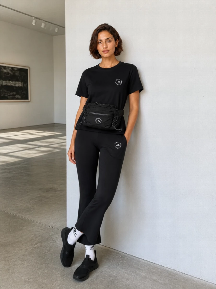 A monochrome Adidas by Stella McCartney set that runs clean and technical, pairing the relaxed black tee with sculpting flared leggings. Slip-on sneakers and a streamlined belt bag keep it practical for studio, travel, or all-day city movement, while logoed socks add just enough detail to feel styled without noise.