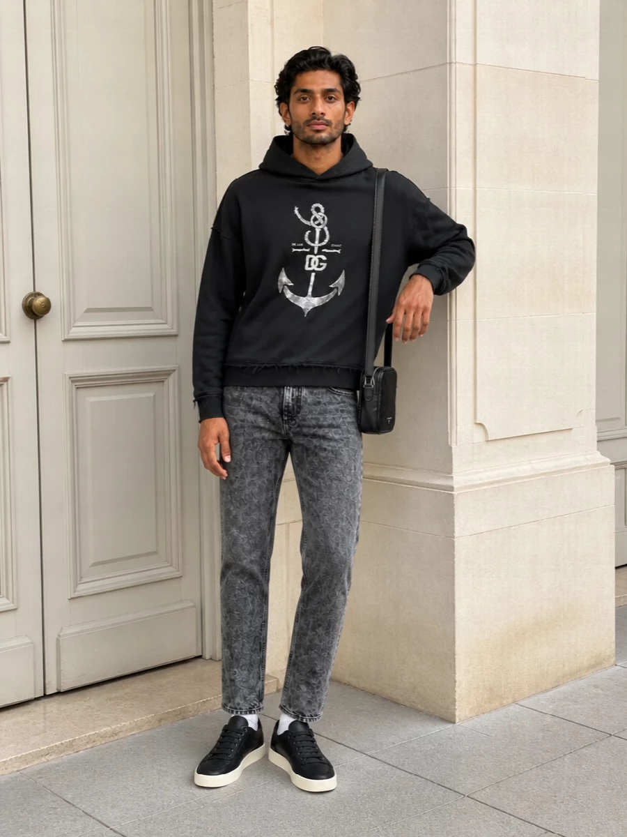 Dolce&Gabbana’s nautical graphic hoodie is grounded with washed charcoal denim for a street-ready mix that feels lived-in but intentional. Black low-top sneakers and a compact crossbody keep the lines clean and athletic, while off-white socks echo the print for a subtle, pulled-together finish. It is an easy off-duty uniform built entirely around dark neutrals and texture rather than loud color.