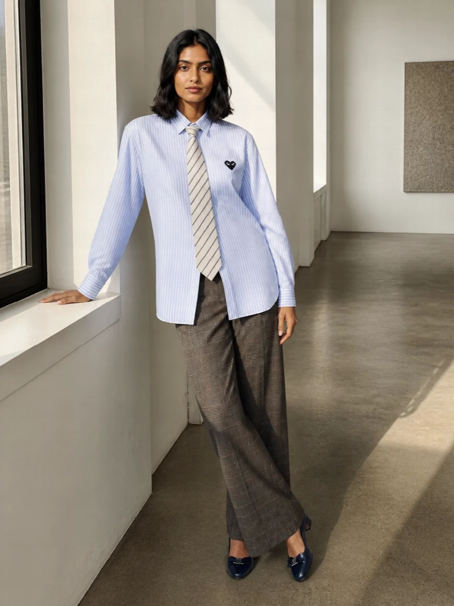 I am building around the tie as a true menswear-prep anchor, so I chose a shirt and trouser combination rather than a dress that would fight the neckwear. The striped Comme des Garçons Play shirt and Pt Torino wide-leg check trouser create a collegiate, slightly androgynous base that lets the buttercream-and-navy tie read intentional, not novelty. Navy Ferragamo pumps and a structured Manu Atelier tote finish it with quiet luxury polish that still feels like it belongs in a seminar room or a smart city coffee meeting.