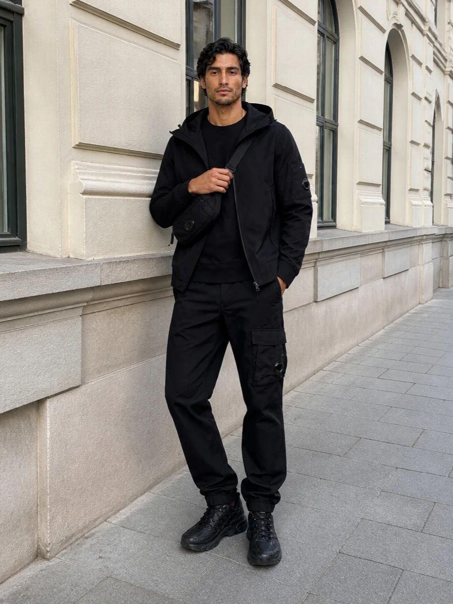 A monochrome C.P. Company rig built around clean technical layers, this outfit leans into urban utility without feeling overdesigned. The straight black cargos, lens-detailed crew and compact crossbody keep the line sleek, while chunky Salomon runners add just enough weight at the ground. It is a quietly assertive city uniform that works from commute to late-night walks with zero effort required from the wearer.