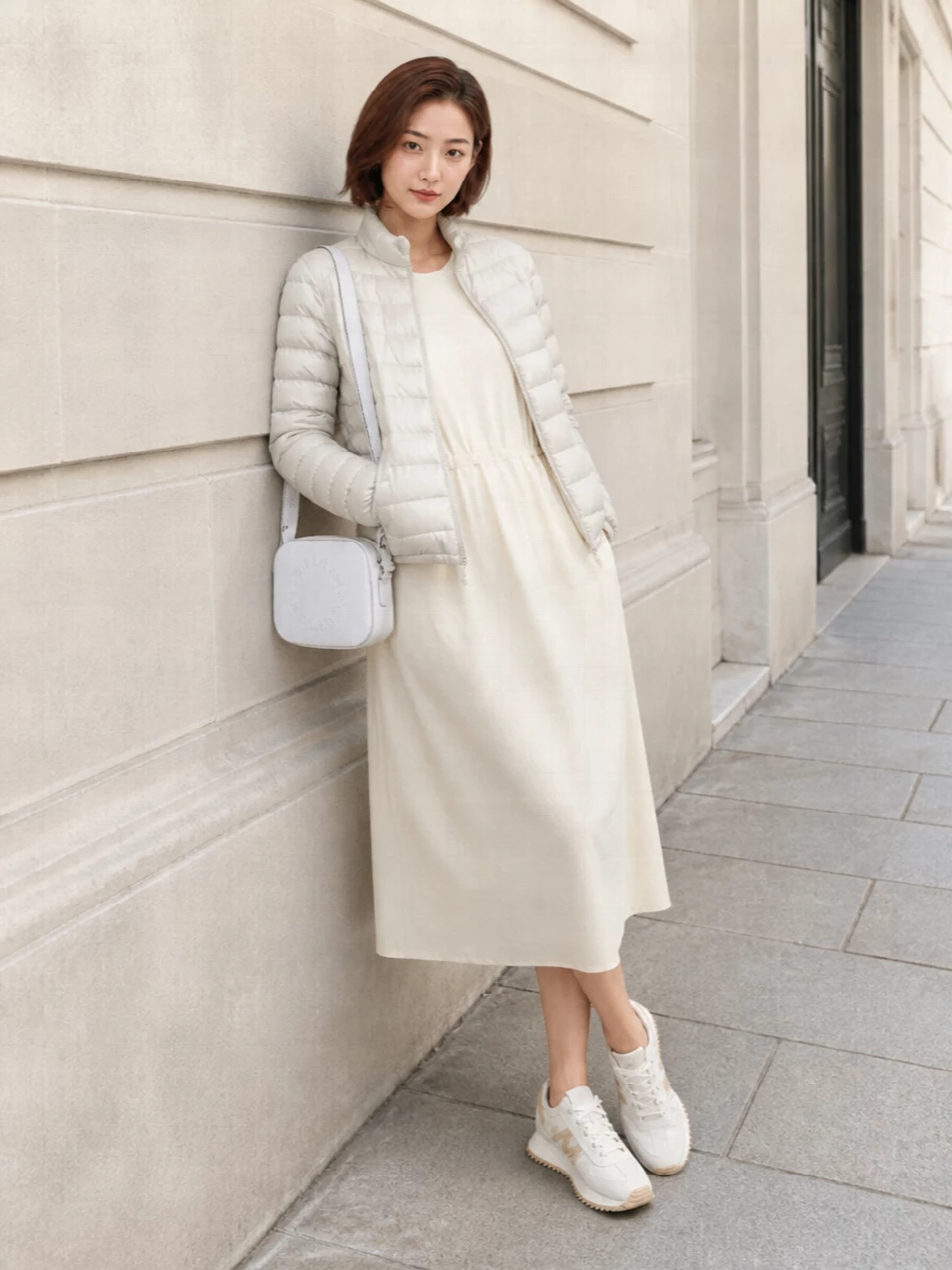 This look leans into a quiet monochrome story: the pale stone Moncler puffer over the softly structured ivory midi T-shirt dress for a cocooning, sport-luxe column. Off-white and beige runners keep it agile and technical, while the compact white crossbody adds just enough structure for city errands or travel days without breaking the serene neutral palette. I chose the dress path to let the outerwear sit over a single, elongated layer, which feels more refined and modern than pairing the short jacket with knee-length shorts here.