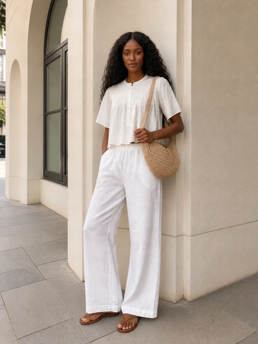 Soft neutrals and airy fabrics keep this wide-leg trouser outfit relaxed yet intentional, perfect for warm days in the city or by the coast. The gently structured ivory blouse shortens the line just enough to flatter the high waist, while tan leather slides and a raffia crescent bag add quiet Mediterranean ease without weighing anything down.