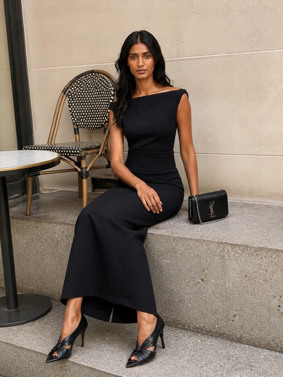 An inky column cinched with a sculpted cummerbund belt creates a precise, long vertical line that feels quietly commanding at night. Cut-out stilettos and a structured black clutch keep the profile sharp and light, all in deep black with subtle metal accents for a pure, architectural evening statement.