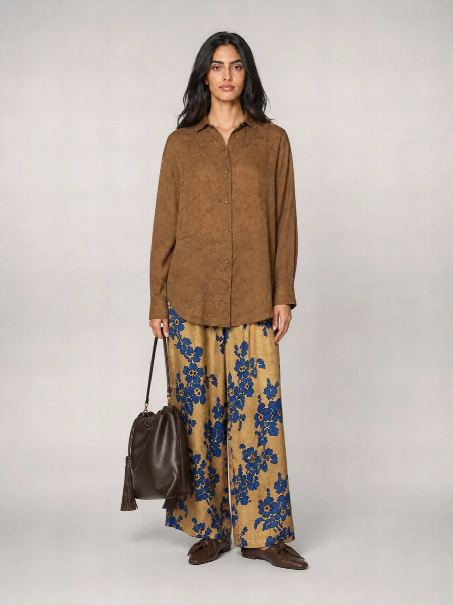 A golden floral wide leg meets a washed caramel shirt for a palette that feels sun-warmed yet moody enough for cooler days. Soft brown leather accents and a slouchy chocolate hobo keep everything grounded and artful rather than precious. The result is relaxed, poetic city dressing that still reads quietly refined.