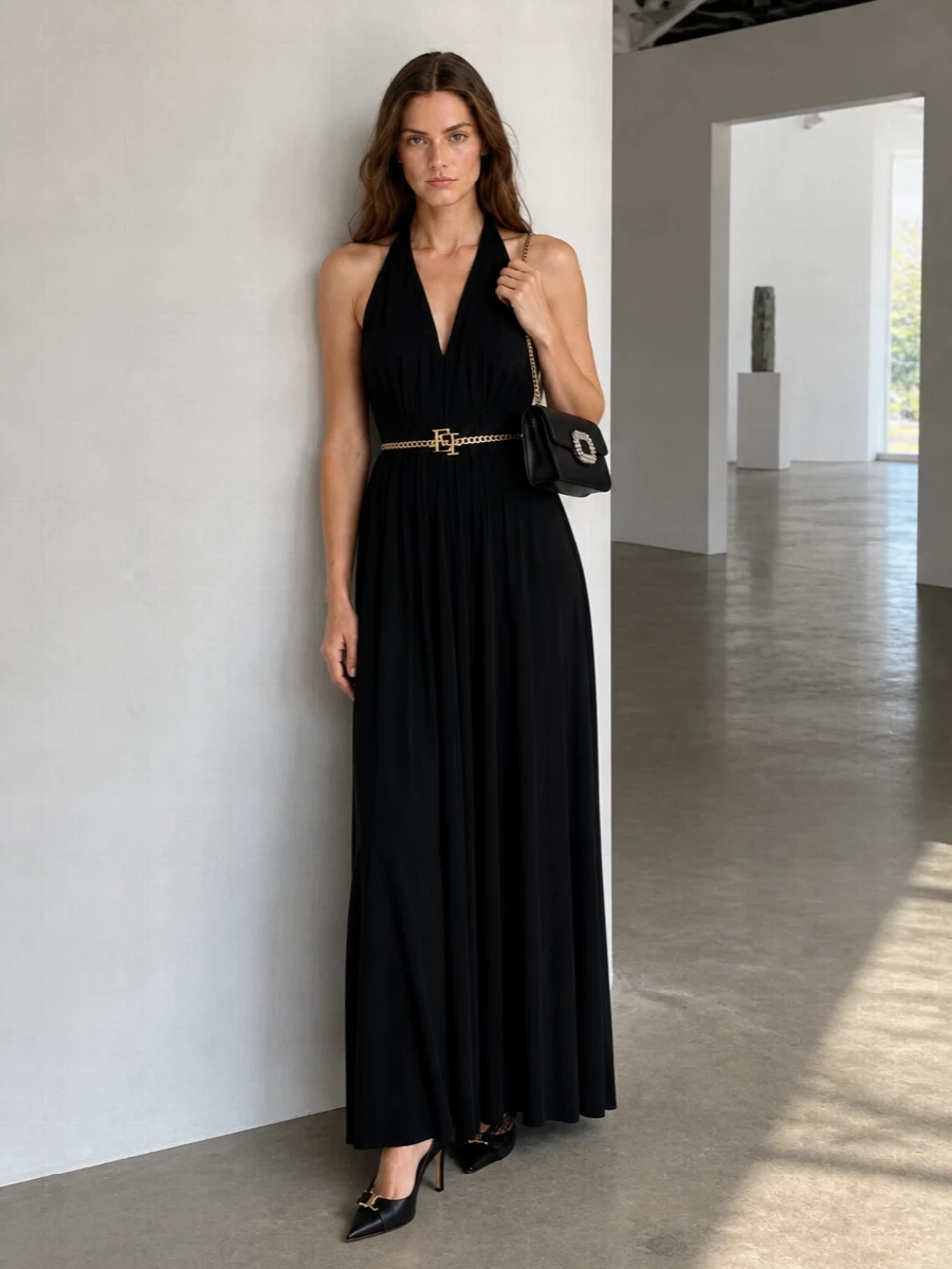 A floor‑sweeping black halter dress becomes pure ceremony paired with razor‑sharp black slingbacks and a jewel‑buckle shoulder bag. The all‑black base, lit only by gold and crystal hardware, reads sensual yet controlled. Every line is long and fluid, so the accessories stay graphic and precise rather than loud.